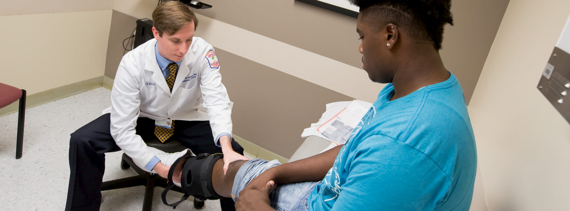 Orthopedic physician examines an injured knee in a brace.